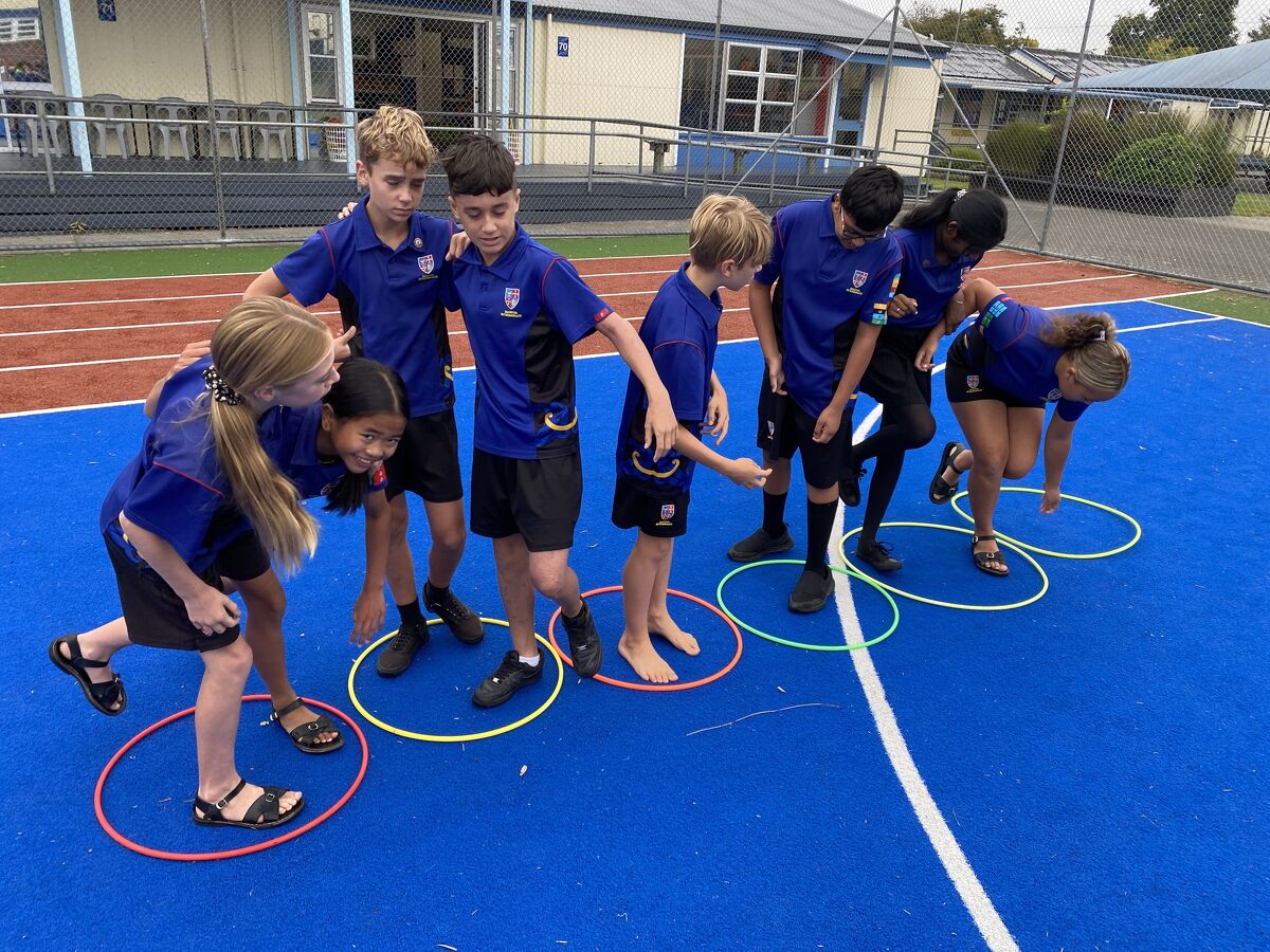 Group of students working together in a team-building activity using hula hoops on the sports court.