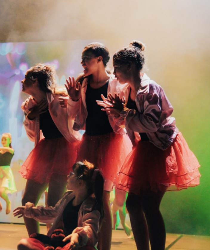 Students performing a dance routine on stage in colourful costumes.