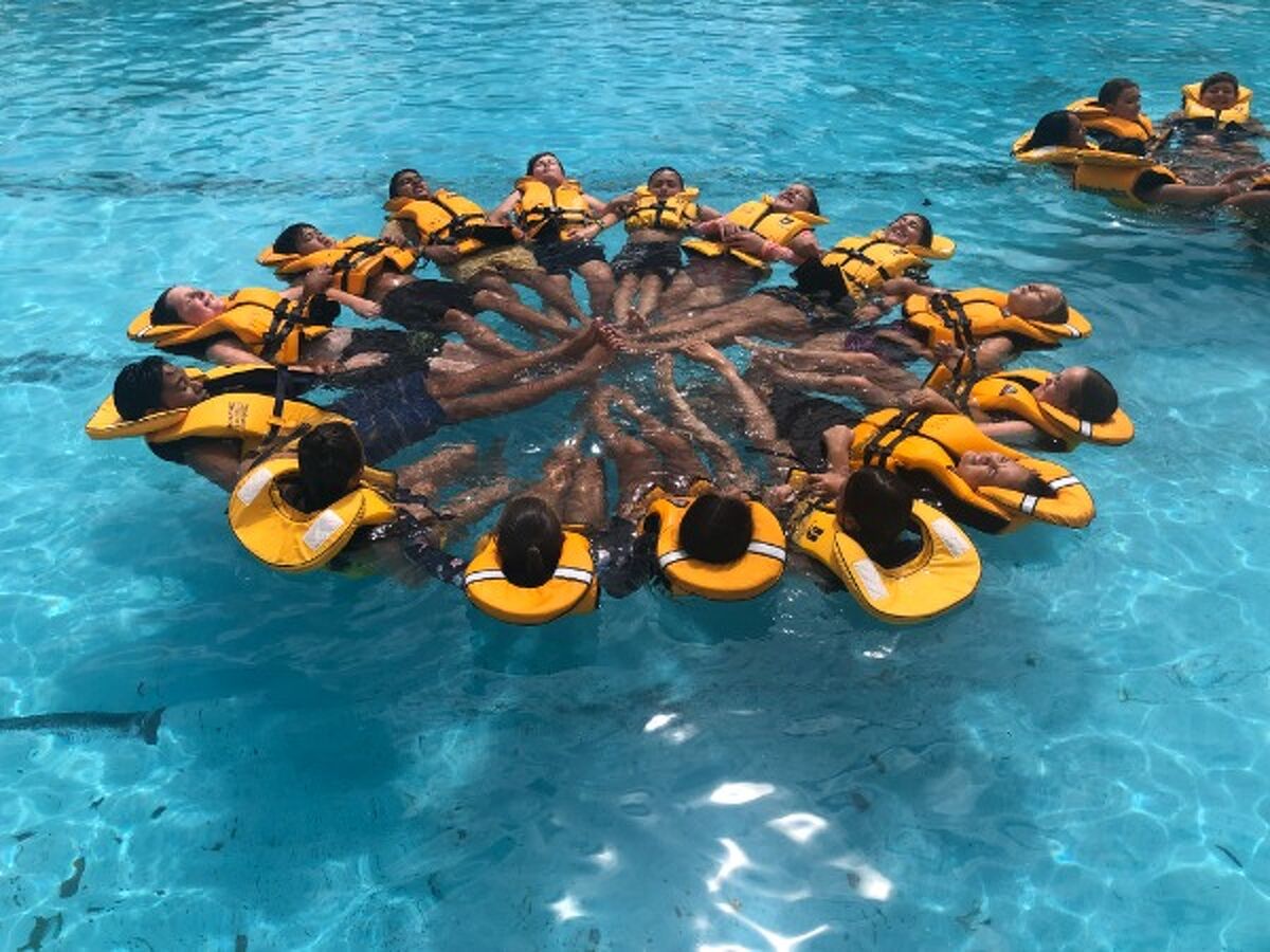 Student wearing life jackets in a pool forming a circle